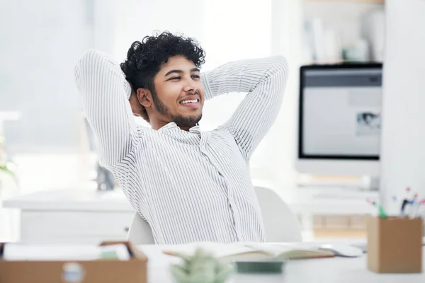 Im so relieved that my deadlines are all done. a young businessman sitting with his hands behind his head while working in an office