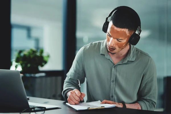 Music gives me motivation to get through the day. a young businessman writing on a notepad in an office at work