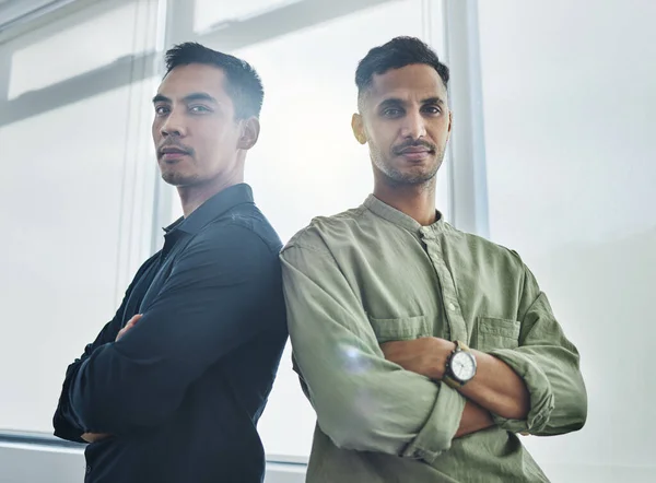Weve got each others backs. Cropped portrait of two handsome young businessmen standing back to back with their arms folded in their office
