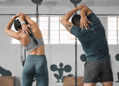 Active, sporty fitness couple stretching or gym partners and friends getting ready to exercise together. Back view of male trainer and female athlete standing and doing warm ups before workout class