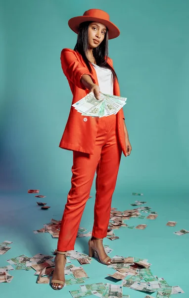 Stylish, trendy and serious woman showing or giving money while standing and posing against blue studio background. Fashionable, beautiful and serious black female giving, spending or donating money.