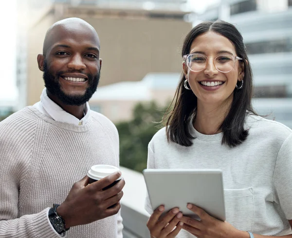 Staying on trend means staying updated. Portrait of two businesspeople drinking coffee and using a digital tablet outside an office