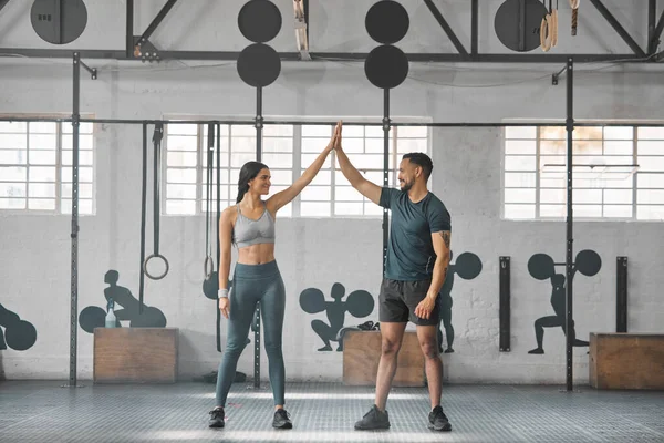 Fit, active and healthy sports athletes training together in gym workout room, living a strong wellness lifestyle. Male and female fitness instructors high five and smiles in physical exercise class.
