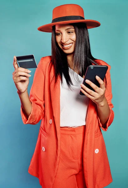 Happy and excited female online shopping, buying with a credit card or paying bills on a phone. Isolated cheerful lady making a purchase on a website, standing in front of blue copyspace background