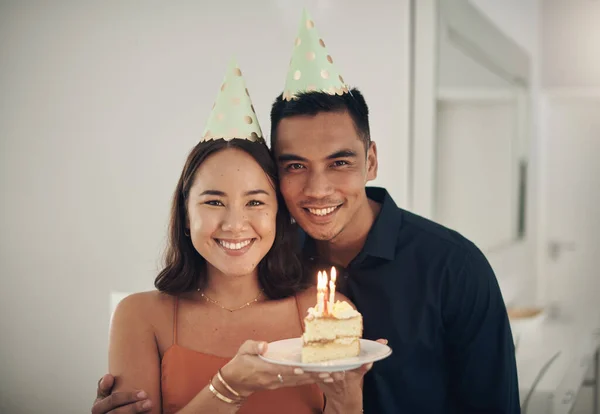 Another year around the sun. a young couple posing with a piece of cake at home