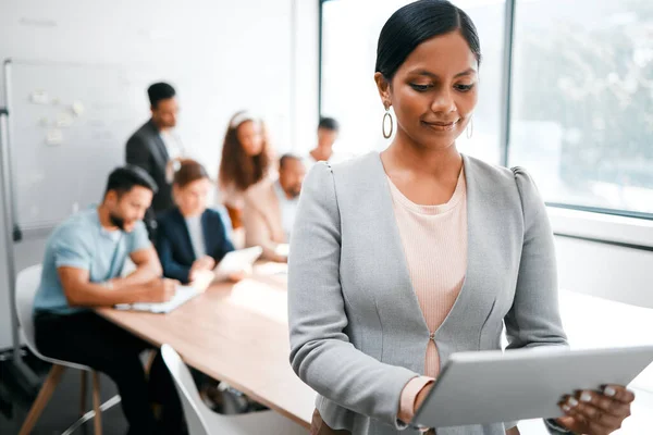 Technology helps me keep track of everything. an attractive young businesswoman attending a meeting in the boardroom with her colleagues in the background