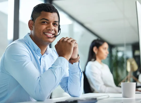 I answer each call with a smile. a young call centre agent sitting in the office with a colleague and wearing a headset