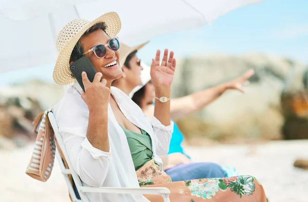 Were having the best day out here. a mature woman sitting alone and using her cellphone during a day out on the beach with friends