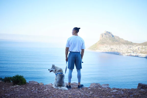 Stopping to take in the view. Rearview shot of an unrecognizable young man and his pet husky taking in the views during their early morning hike in the mountains