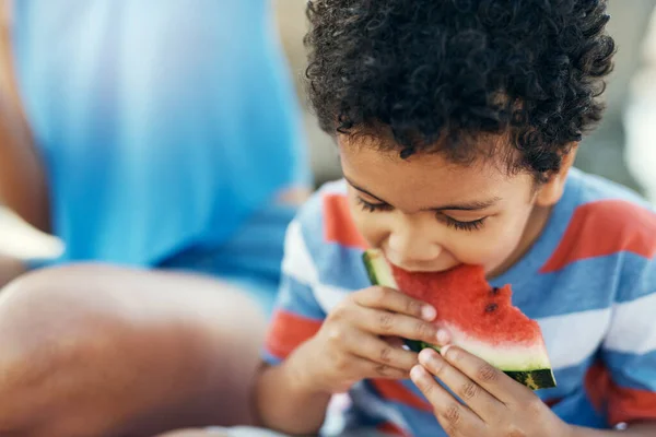 Mom always packs my favourite food. a young boy enjoying a piece of watermelon outside