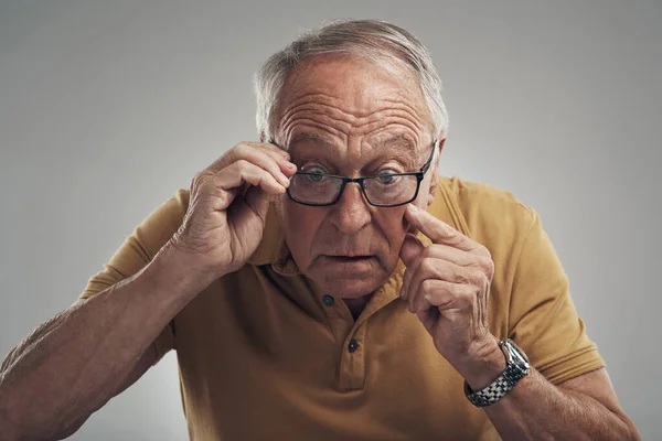 Im definitely getting old. Studio shot of an elderly man adjusting his spectacles against a grey background
