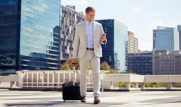 Getting work done on the go. a young businessman using a cellphone while walking with a suitcase in the city