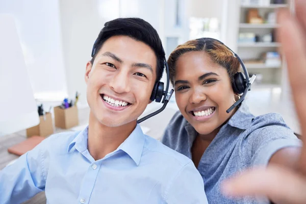 Selfie of diverse call center agents or colleagues having fun together at the office. Male and female customer service coworkers take a picture or a photo smiling in the workplace.