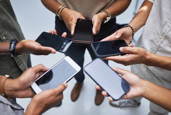 Connecting to whats new in the business world. High angle shot of a group of unrecognisable businesspeople using their cellphones in an office