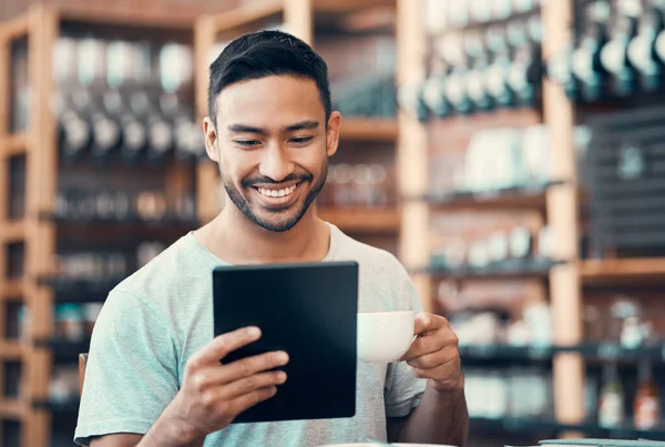 Happy, relaxed and carefree man reading social media news on a tablet while enjoying coffee. Young casual guy replying to emails, browsing the internet or subscribing to online dating app at a cafe.