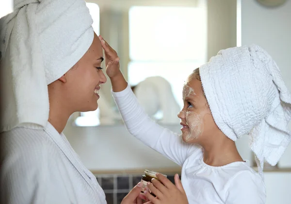 Mother and daughter bonding and spending time together on a spa day at the family home. Little girl applying face cream while smiling and having fun. Happy mom and child doing a skin facial.