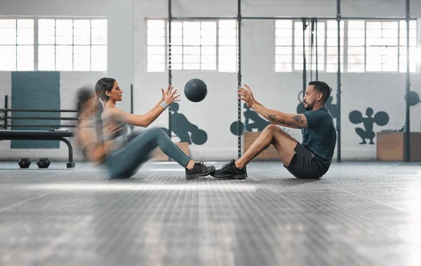 Active, sporty fitness couple or gym partners training together, doing abs exercises by throwing a weighted slam ball. Male trainer and female athlete in motion focused on workout session or class