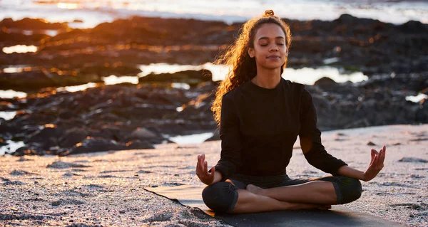 Gratitude brings positive change. an attractive young woman sitting alone on a mat and meditating on the beach at sunset