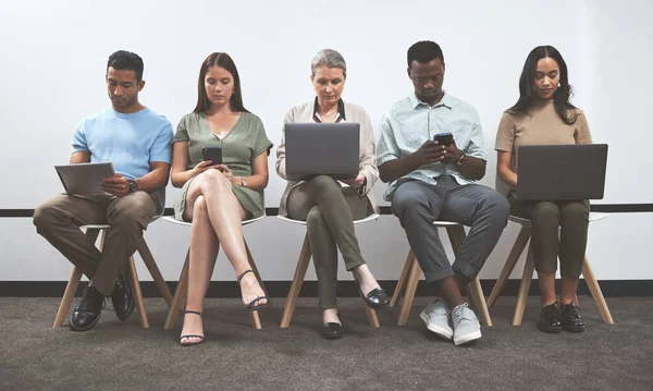 Prepare well so you can do well. a group of businesspeople using digital devices while sitting together in a line against a white wall