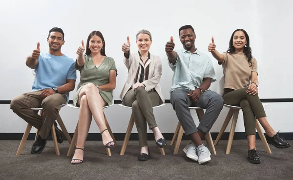 Believe in yourself and you will succeed. Portrait of a group of businesspeople showing thumbs up while sitting together in a line against a white wall