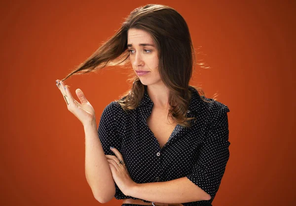 What am I going to do with you. an attractive young woman standing alone against a red background in the studio and touching her hair