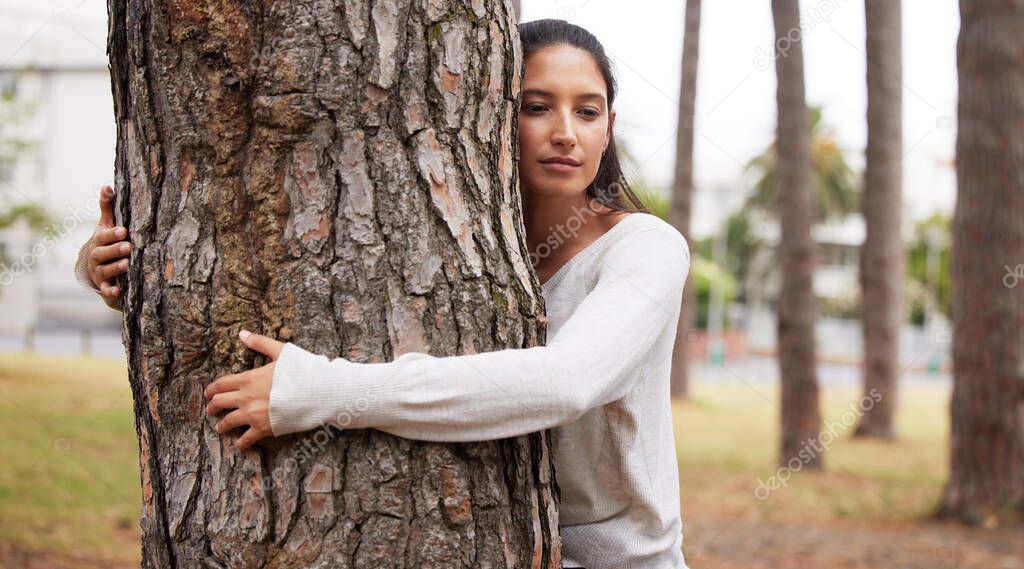 An embrace with centuries. a young female hugging a tree in a park