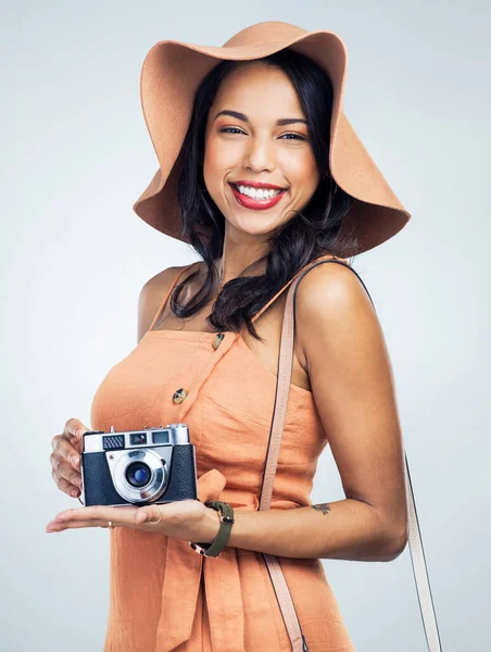 The one thing you need when traveling is your camera. Studio shot of a beautiful young woman holding a camera while standing against a white background
