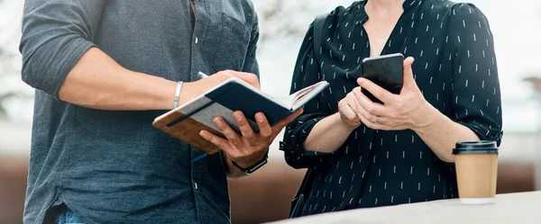 You dont always get what you wish for, you get what you work for. two unrecognisable students looking at a notebook and using a mobile phone outside on campus