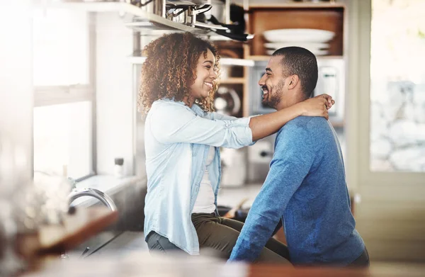 Young, in love and happy couple talking, hugging and having fun in a kitchen at home. Lovers embracing, enjoying time together while bonding. Partners being affectionate and having a romantic moment.