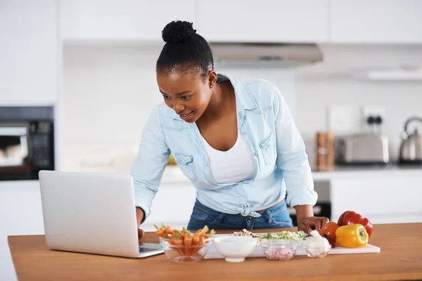 Im sure Ill find a easy recipe online. a young woman using a laptop while cutting vegetables at home