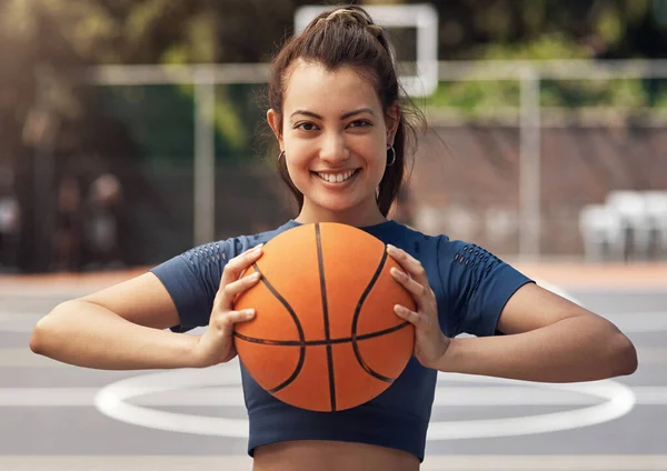 Playing basketball can boost your confidence. Portrait of a sporty young woman holding a basketball on a sports court