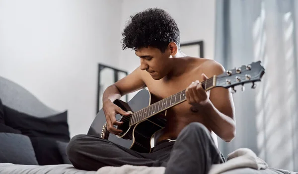 Good music makes your heart beat along with it. a young man playing the guitar in his bedroom at home