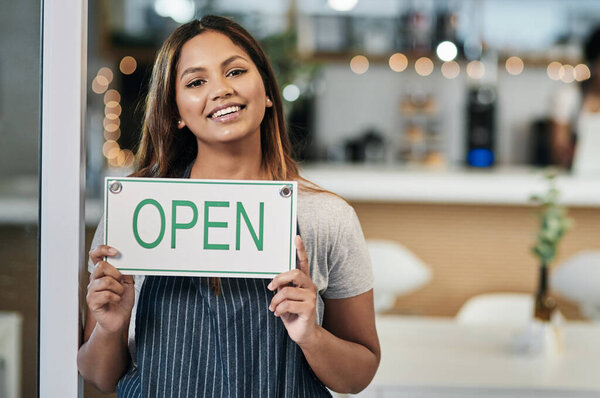 It was always my dream to open this little cafe. Portrait of a young woman holding an open sign in a cafe