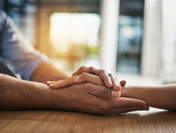 Kindness, support and trust between two people holding hands while sitting at a table together. Closeup of two people talking through hard time or discussing a problem while showing concern and love.