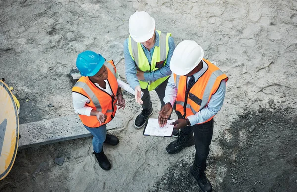 The hardest work happens out in the field. a group of builders going over building plans at a construction site