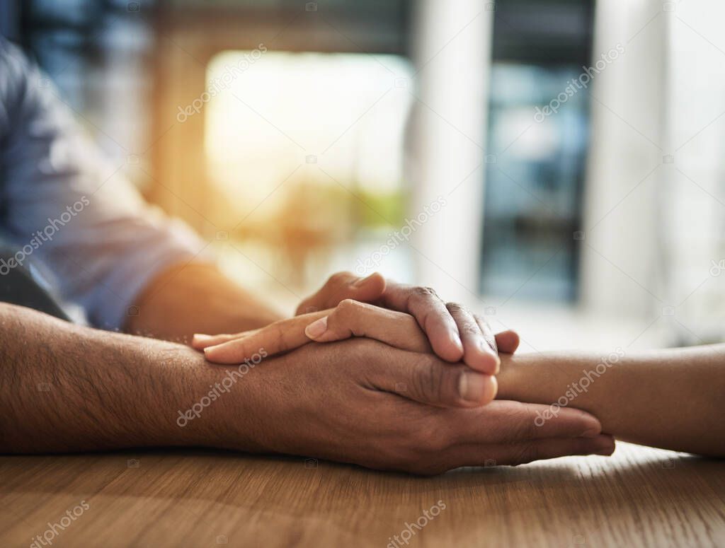 Kindness, support and trust between two people holding hands while sitting at a table together. Closeup of two people talking through hard time or discussing a problem while showing concern and love.