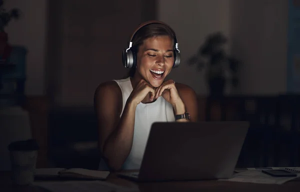 The perfect podcast to take her through the night. a young businesswoman using headphones and a laptop during a late night in a modern office