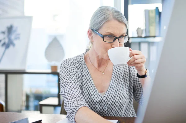 Sipping on success. a mature businesswoman drinking tea while working on a computer in an office