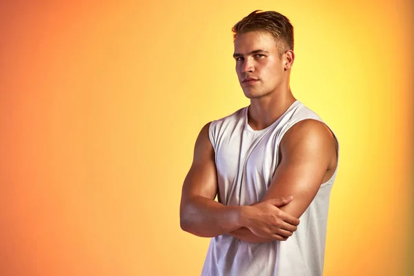 Fitness is a confidence builder. Studio portrait of a handsome young male athlete standing with his arms folded against an orange background