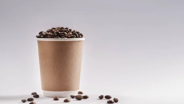 Lets meet for coffee. Studio shot of a paper cup filled with coffee beans against a grey background