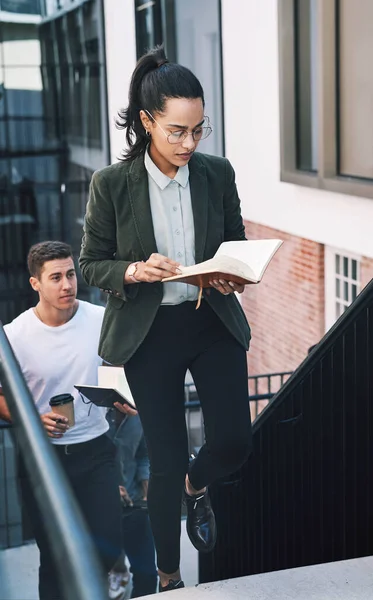 Slow and steady wins the business race. a young businesswoman looking at her notebook while walking up the stairs in a modern workplace