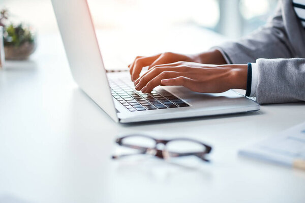 Closeup of hands of a business person typing on a laptop, browsing the internet online and finishing a proposal while sitting at a table in an office at work. One employee networking on the web.