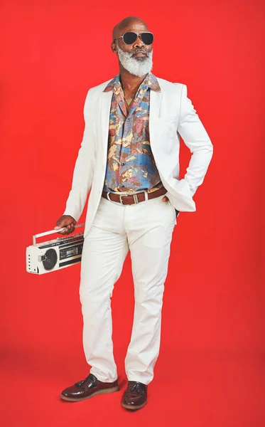 People hear me coming before they see me. Studio shot of a senior man wearing vintage clothing while posing with a boombox against a red background