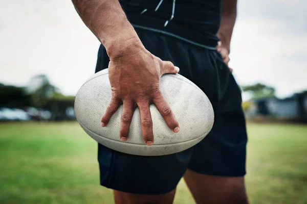 Playing with this ball is his favourite thing. an unrecognizable rugby player holding a rugby ball on the field during the day