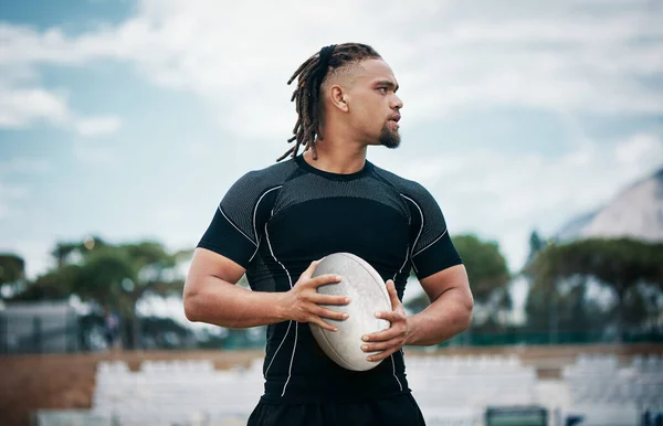 Rugby is his profession. a handsome young rugby player holding a rugby ball while standing on the field