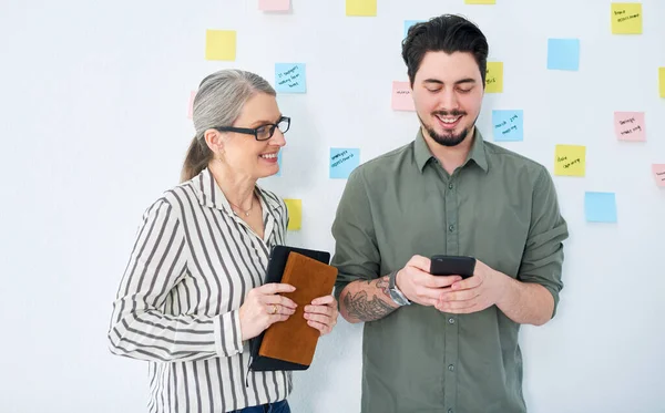 Getting some incoming texts with good news. two businesspeople using a cellphone together in an office