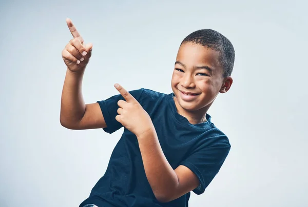 Check it out, yo. Studio shot of a cute little boy pointing against a grey background
