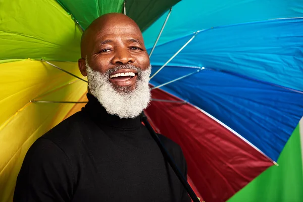 Keep yourself covered. a senior man posing with a colorful umbrella over his head