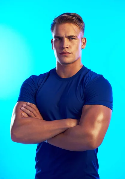 Its a matter of confidence. Studio portrait of a handsome young male athlete standing with his arms folded against a blue background