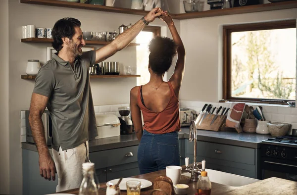 Happy, romantic and interracial couple dancing and having fun while bonding in kitchen at home. Carefree and energetic loving couple feeling cheerful while sharing a dance and enjoying time together.